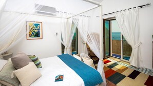 Ein Schlafzimmer mit Bett, Nachttisch, Vorhängen und Meerblick.