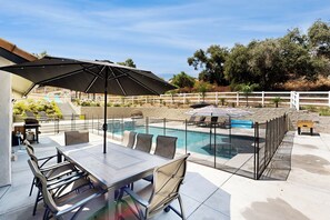 A poolside area with a dining table, chairs, and a large umbrella. - 4BR Wine Country Home w/ Views, Pool, Hot Tub (Temecula)