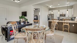 A modern kitchen with white cabinets, a microwave, and a refrigerator. There is a dining area with a round table and chairs. - Home Gym & Sauna! Luxe Lehigh Acres Family Home (Lehigh Acres)