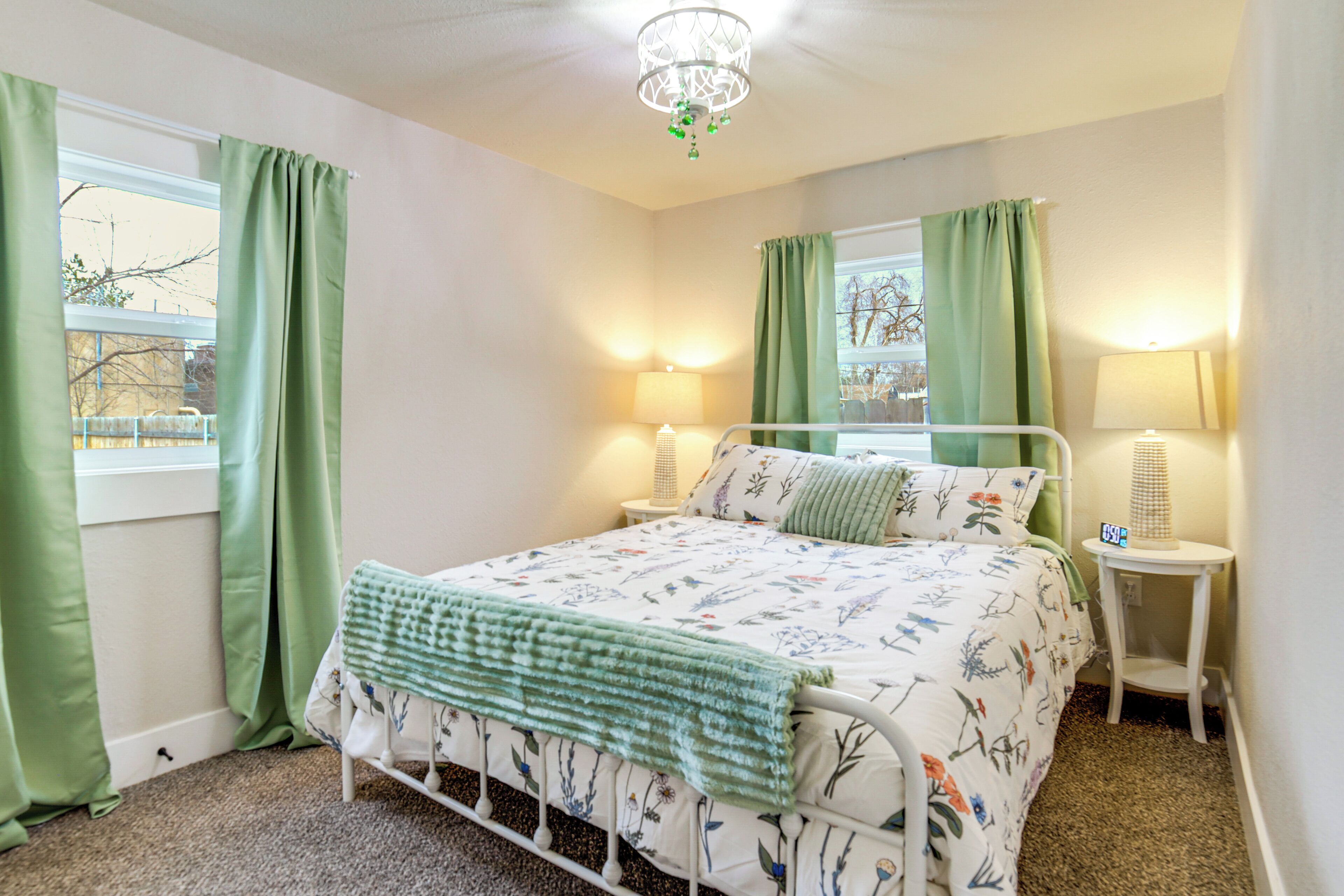 A bedroom with a bed, two bedside lamps, a small table, and a window with curtains.