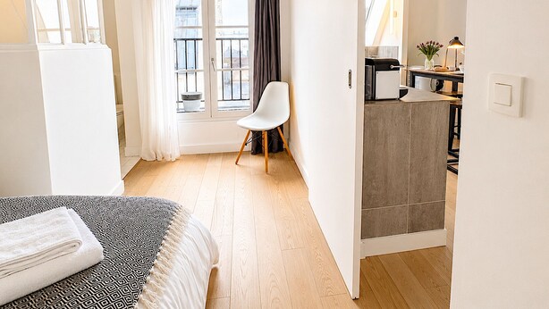 Una habitación de hotel moderna con una cama, una silla, kitchenette y vistas a la ciudad.