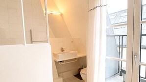 Un baño con ducha, lavamanos e inodoro, una ventana con cortinas y vistas al exterior.