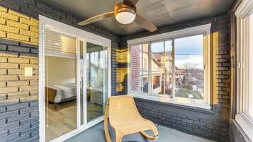 A room with a glass door leading to a balcony, a ceiling fan, and a view of the neighborhood.