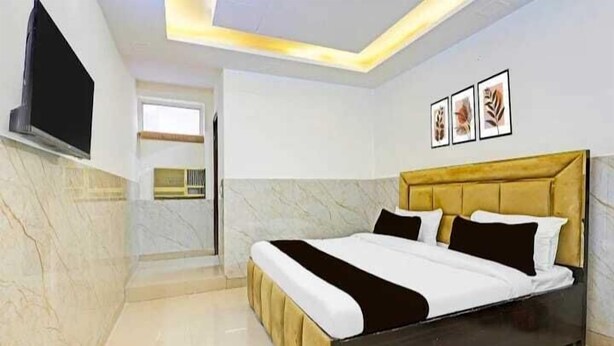 A modern bedroom with a large bed, a TV mounted on the wall, and a small kitchen area. - Roomshala Hotel Smart  (New Delhi)