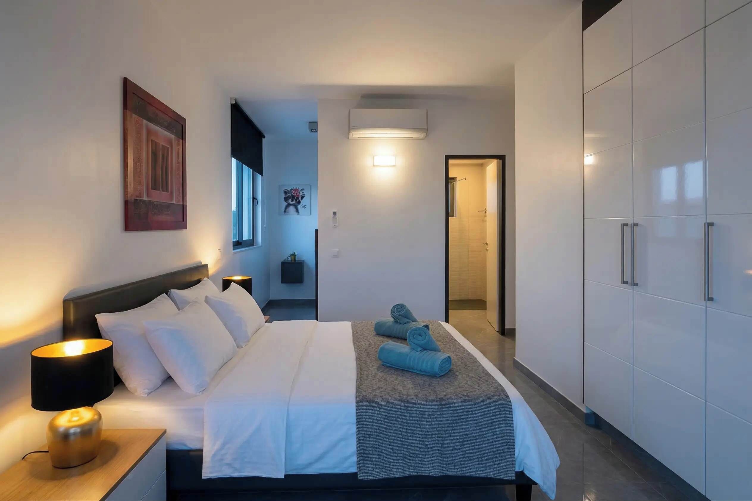 Ein Hotelzimmer mit Bett, Nachttischlampe, Wandbild und Kleiderschrank.