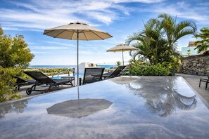 Ein Poolbereich mit Liegestühlen, Sonnenschirmen und Blick auf den Ozean.