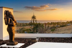 Eine Statue auf einem Sockel mit Blick auf eine Küstenlandschaft und einem wolkenlosen Himmel.