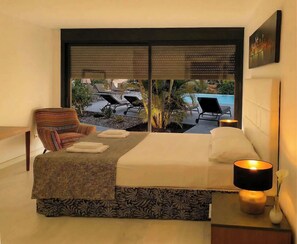Ein Schlafzimmer mit Bett, einem Sessel, einem Nachttisch mit Lampe und Blick auf einen Außenpool.