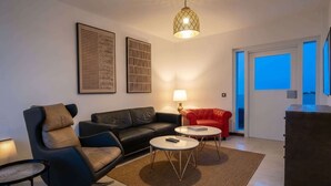 Una sala de estar moderna con un sofá de cuero negro, un sillón rojo, dos mesas de centro redondas, una lámpara de pie y obras de arte en las paredes.