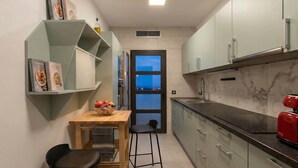 Una cocina moderna con una mesa de madera, dos sillas negras, un cuenco de fruta y un hervidor rojo.