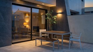 Un área de comedor moderna al aire libre con pared de vidrio, una mesa, sillas y un banco.