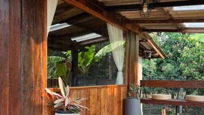 A wooden deck with a table and chairs, surrounded by potted plants and a view of greenery. - Room-boutique Cabin · Peaceful Mountain (Chiang Dao)