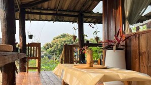 An outdoor wooden deck with a table and chairs, surrounded by potted plants and a view of greenery. - Room-boutique Cabin · Peaceful Mountain (Chiang Dao)