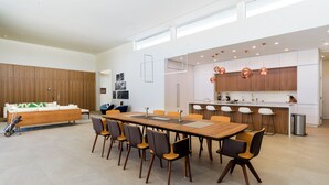 A modern kitchen with a central island, a dining area with a long table and chairs, and a sofa against a wooden wall. - Above Palm Springs Sanctuary | Mountain Views | Pool & Spa | Old Las Palmas (Palm Springs)