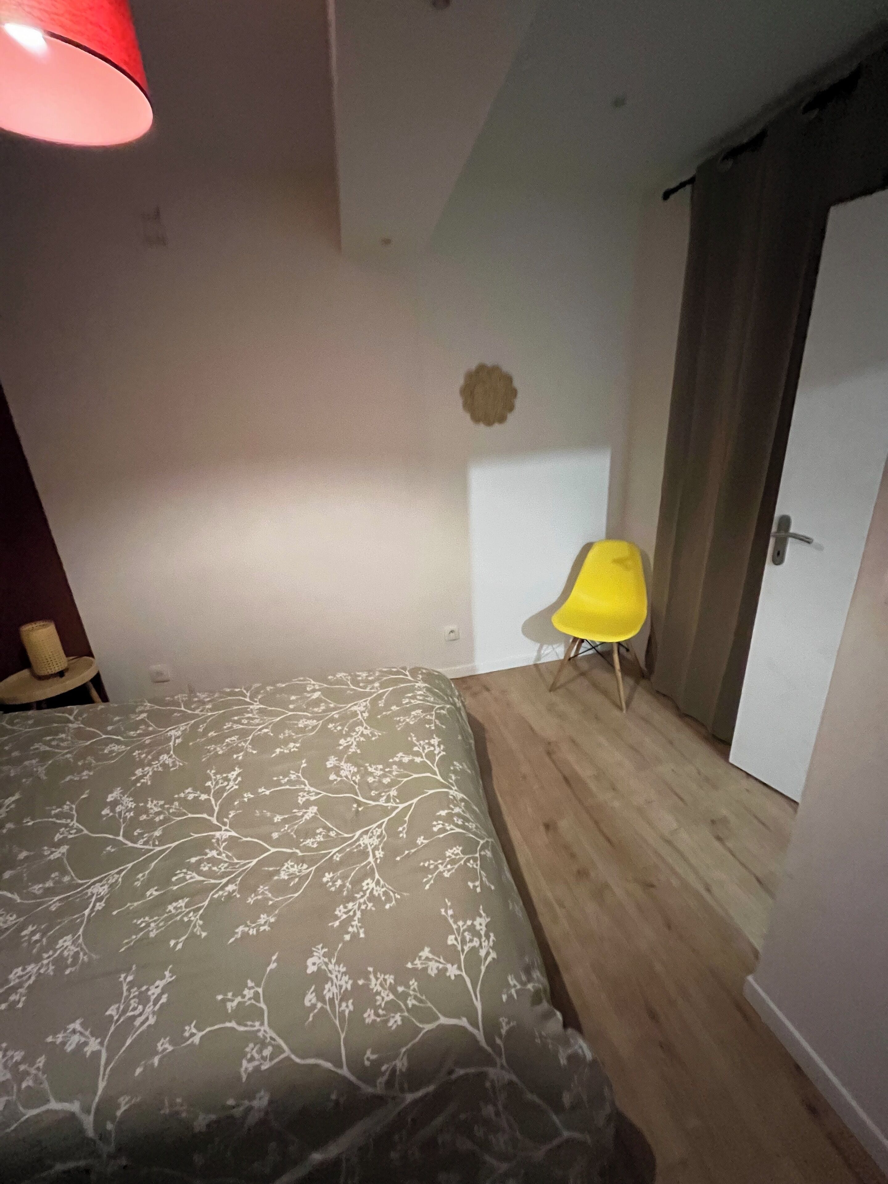 Une chambre à coucher avec un lit, une chaise jaune, une porte et une lampe rouge.