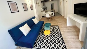 Ein modernes Wohnzimmer mit einem blauen Sofa, einem gemusterten Teppich und einem Fernseher auf einem weißen Schrank.