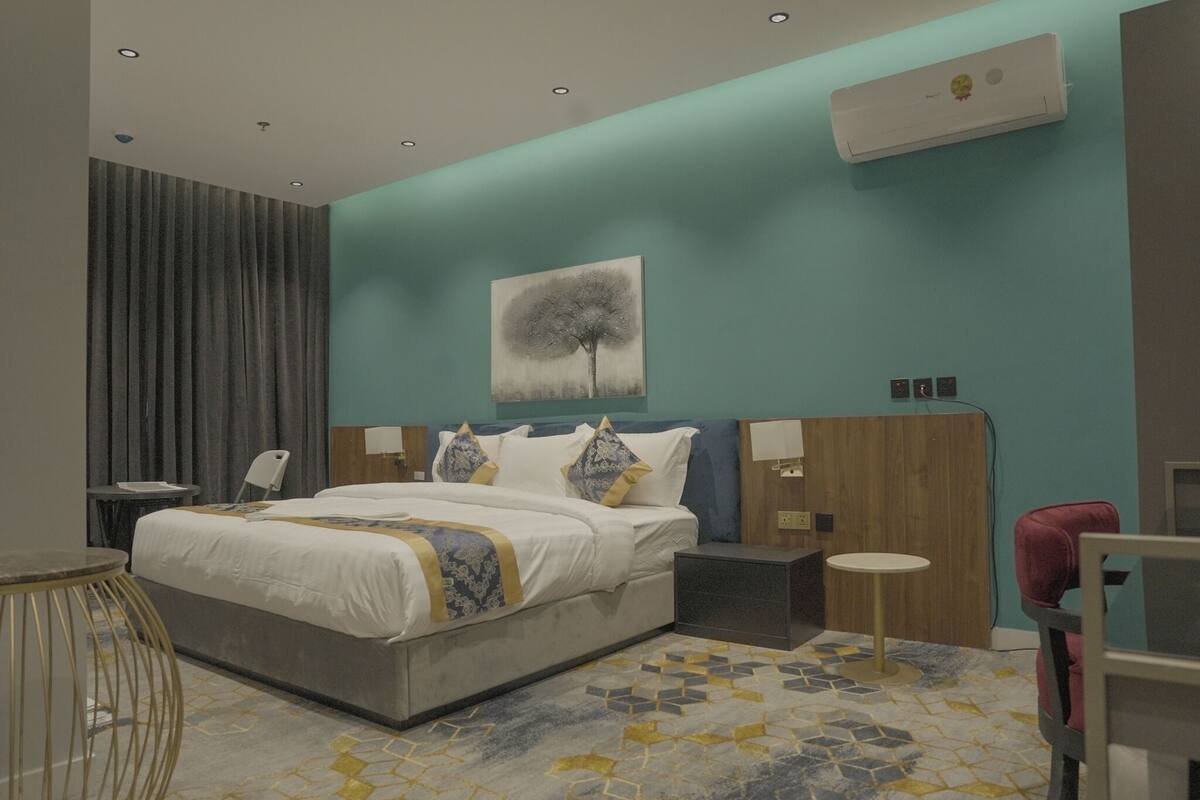 A modern hotel room with a large bed, a desk, a chair, and a small table.