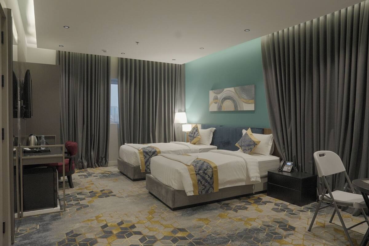 A hotel room with two beds, a desk, a chair, and a small table.