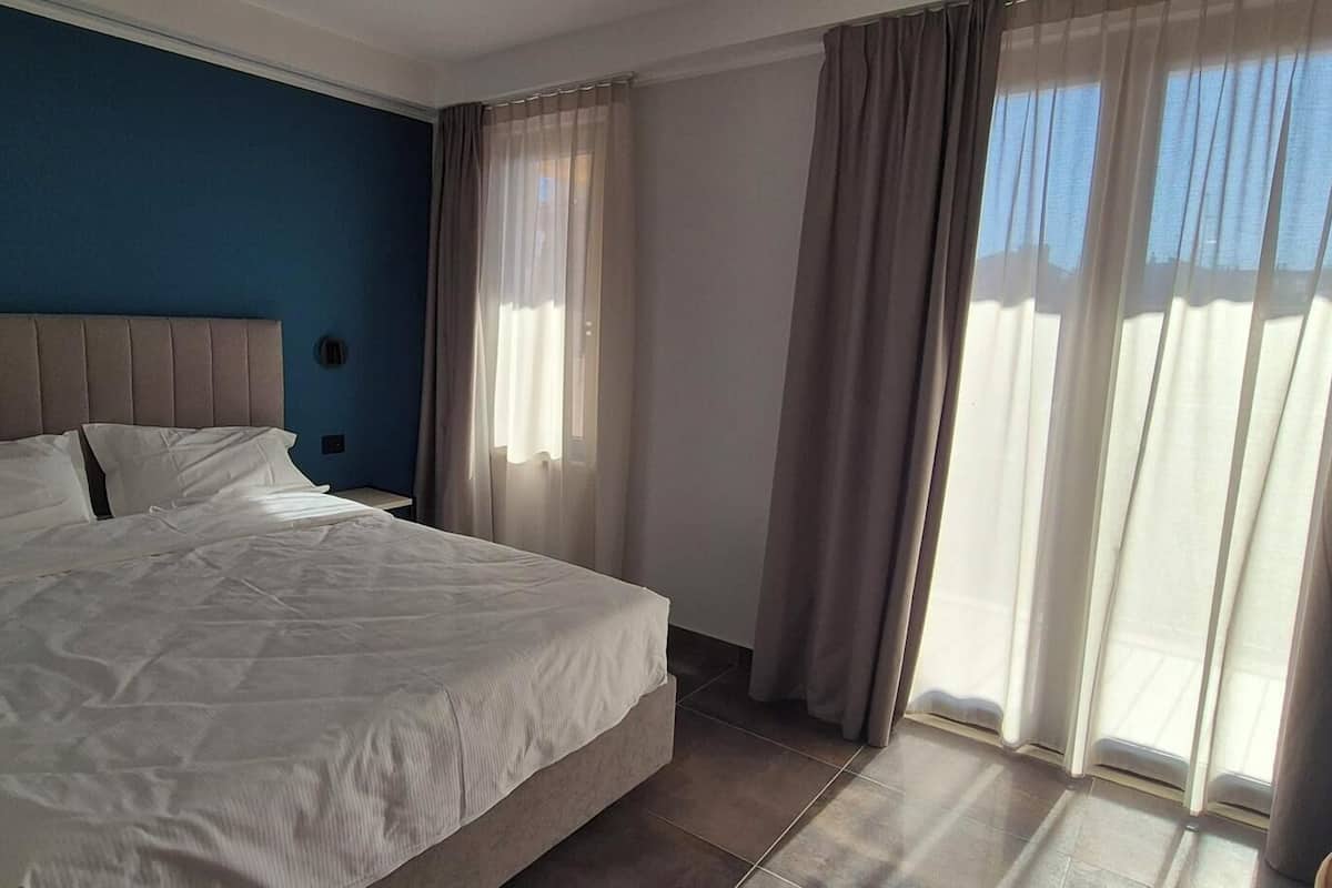A hotel room with a bed, curtains, and a view of the outdoors.