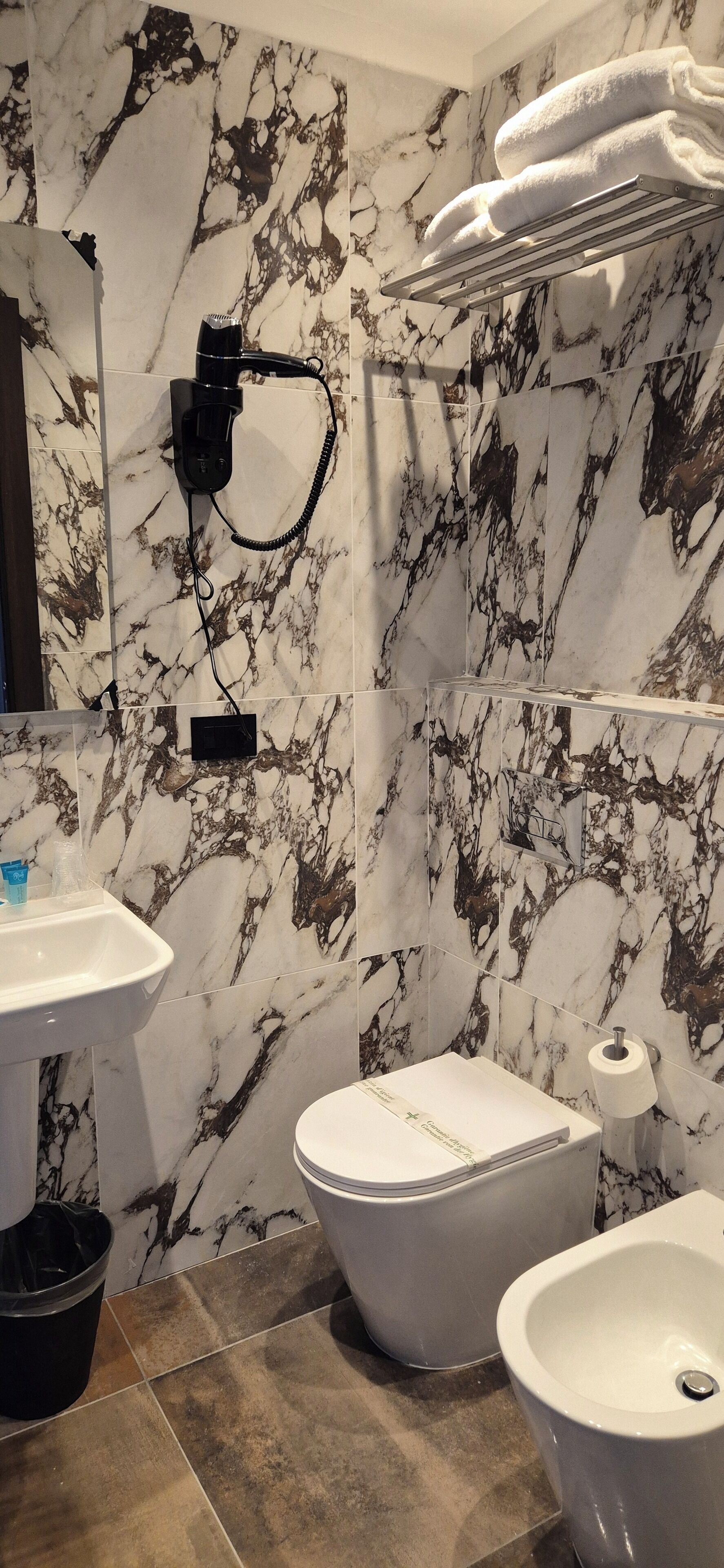 A bathroom with marble walls, a sink, a toilet, and a bidet.
