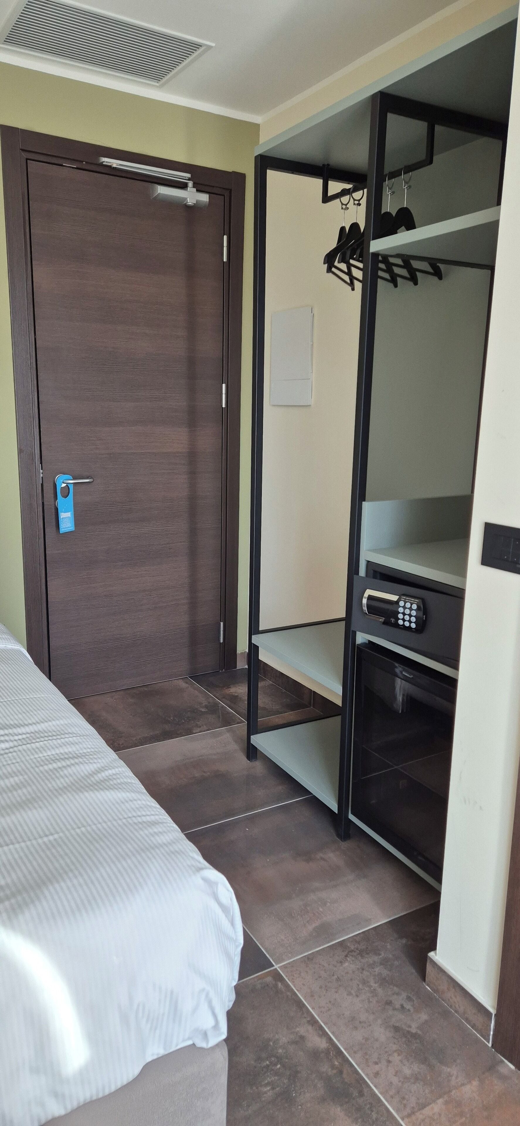 A bedroom with a bed, a wardrobe with a built-in heater, and a small shelf.