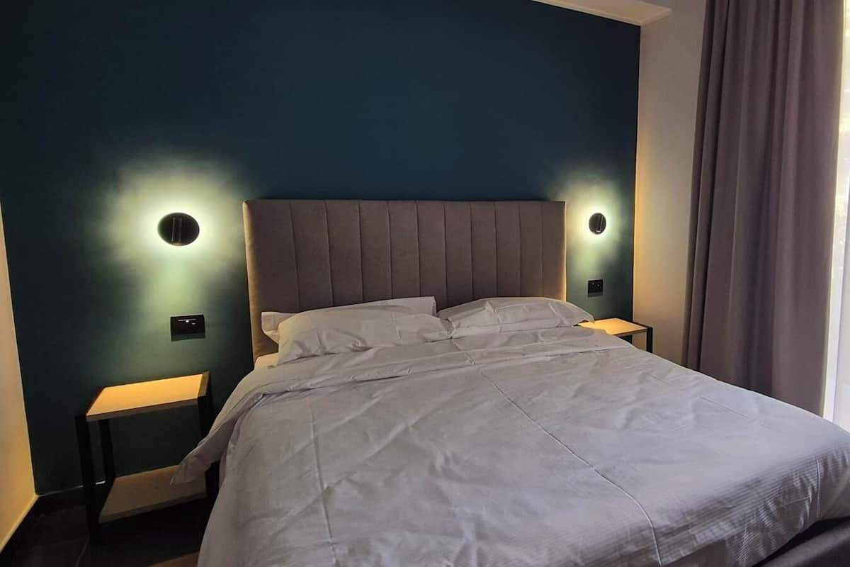 A neatly made bed with a grey headboard and pillows, two bedside tables with lamps, and a window with curtains.