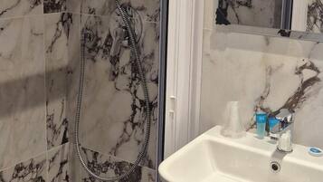 Un bagno con doccia, lavandino e parete rivestita in marmo.