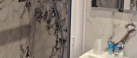 Un baño con ducha, lavamanos y pared con azulejos de mármol.