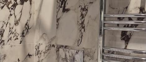 Un baño con paredes de mármol, un inodoro, un lavamanos y un perchero con toallas dobladas.