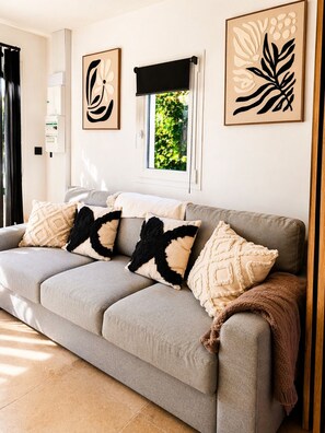 A grey sofa with patterned cushions, a window with a view of greenery, and abstract art on the walls. - 🌿 Renovated dovecote with SPA & Pyrenees view - Pets welcome (Marliac)