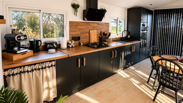 Una cucina moderna con piano di lavoro in legno, mobili neri, una macchina per il caffè e una finestra vista alberi.