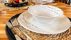 Un tavolo da pranzo apparecchiato con piatti, bicchieri e posate, con un sottopiattino in tessuto e una parete decorativa sullo sfondo.