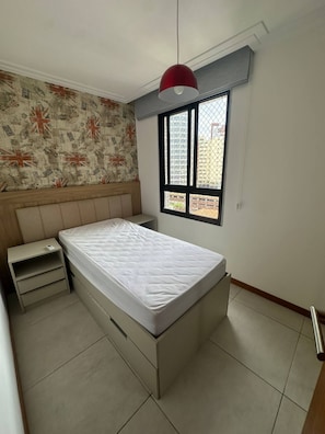 A bedroom with a bed, a nightstand, a window with a view of buildings, and a patterned wallpaper. - Porto Gold Way Apart Porto da Barra Beach à 450m Away (Salvador)