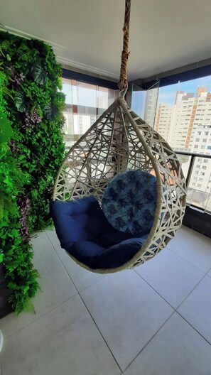 A hanging chair with a blue cushion in a room with a green wall and a view of buildings. - Porto Gold Way Apart Porto da Barra Beach à 450m Away (Salvador)