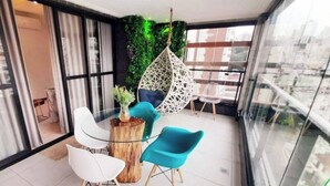 Un balcon moderne avec une table en verre, des chaises blanches et bleues, un fauteuil suspendu et un mur végétal.