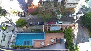 Vue aérienne d’un quartier résidentiel avec une piscine, un petit patio doté de tables et de chaises, et plusieurs voitures garées.