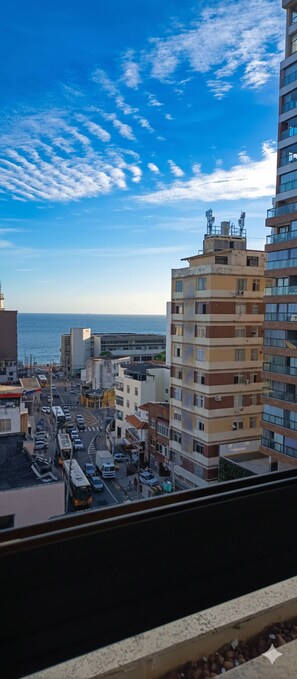 Un immeuble de grande hauteur, avec de nombreux étages, offrant une vue sur la mer et donnant sur une rue animée où circulent de nombreux véhicules.