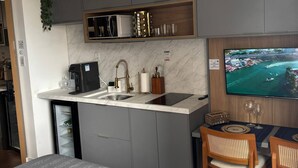 Une cuisine compacte équipée d’un four à micro-ondes encastré, d’une machine à café et d’un évier. Un petit coin repas avec une table et des chaises est à disposition, ainsi qu’un téléviseur fixé au mur.
