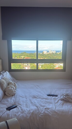 Une chambre dotée d’une grande fenêtre donnant sur un paysage urbain et la mer.