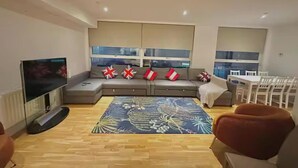 Una sala de estar moderna con un sofá, un televisor de pantalla plana, un comedor con sillas y una alfombra estampada.