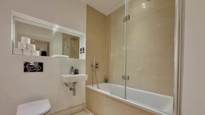 Un baño moderno con inodoro, lavamanos y ducha con mampara de vidrio.