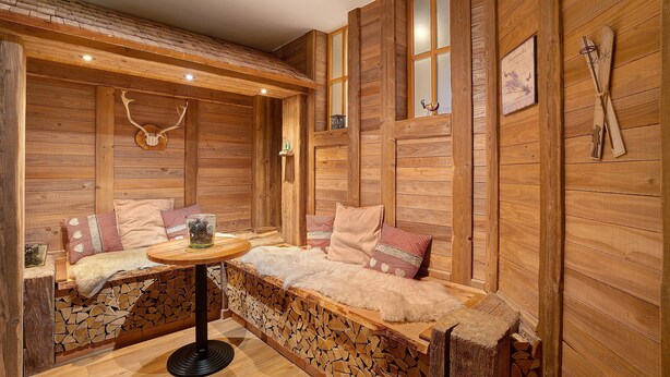 Interior de una cabaña de madera con sofá, una mesa y chimenea.