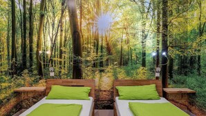Habitación temática de bosque con dos camas, cabecera de madera y vista a un bosque denso.