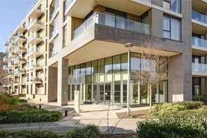Een modern woongebouw met meerdere verdiepingen, balkons, een grote glazen entree en een aangelegde omgeving.