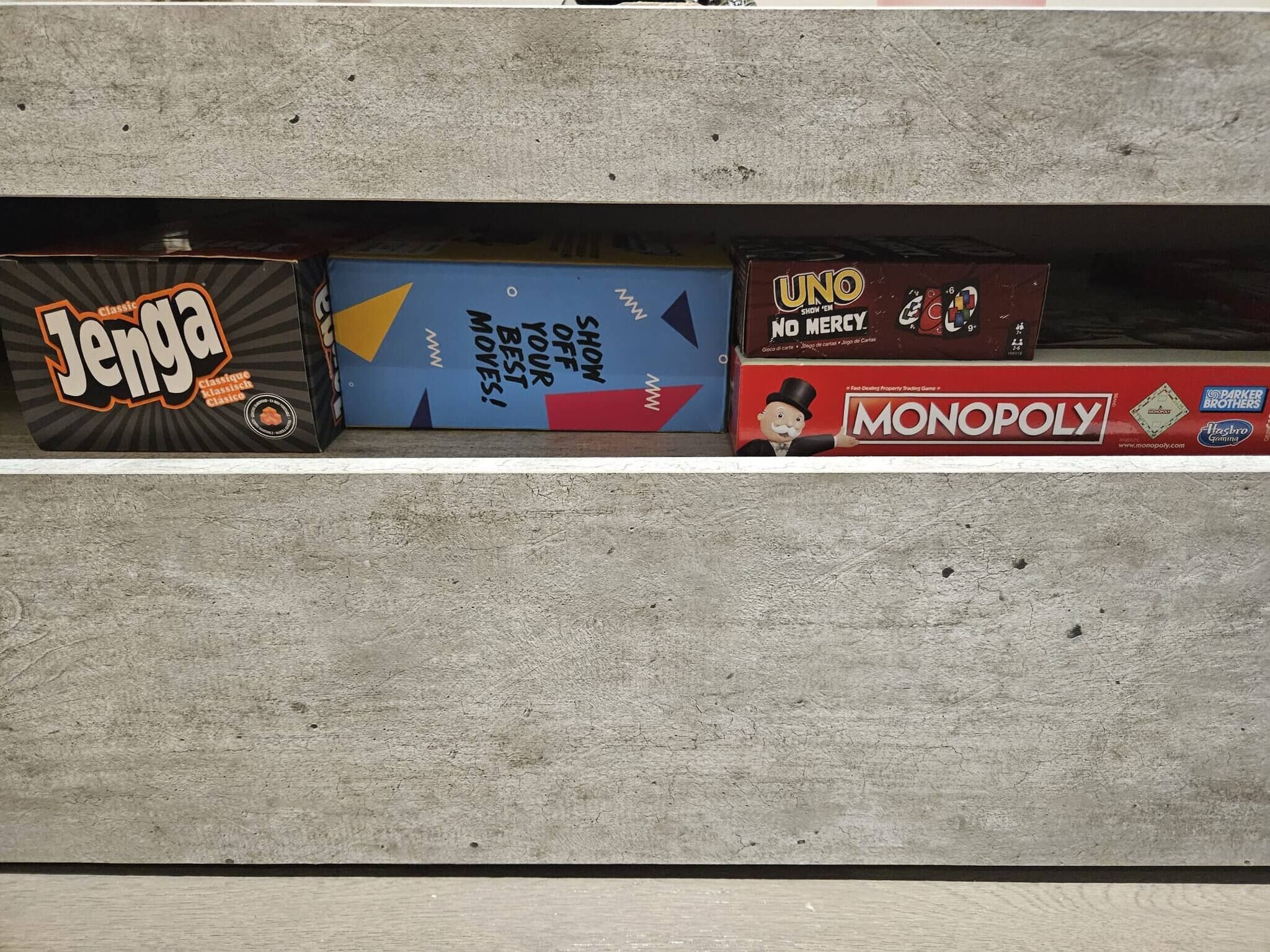 Ein Regal mit drei Brettspielen: Jenga, Monopoly und UNO.