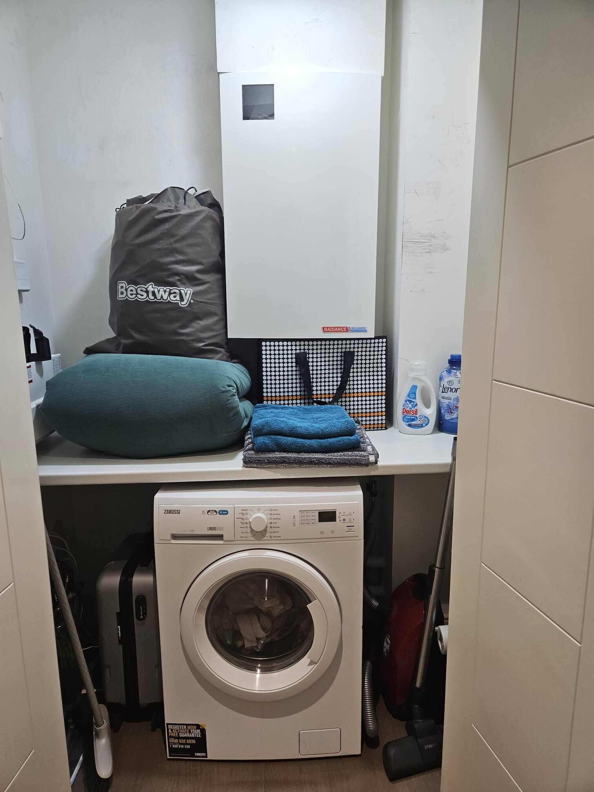 A laundry area with a washing machine, a drying rack, a towel, a bag, and cleaning supplies.