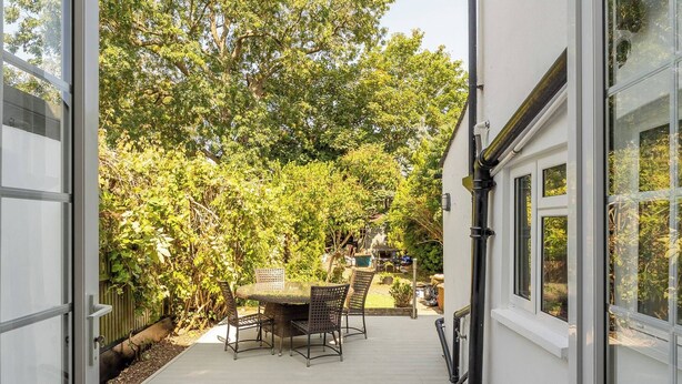 A covered patio with a table and chairs, leading to a garden area with trees and a fence. - Elegant 3BR Victorian Retreat, Free Parking (Kingston Upon Thames)