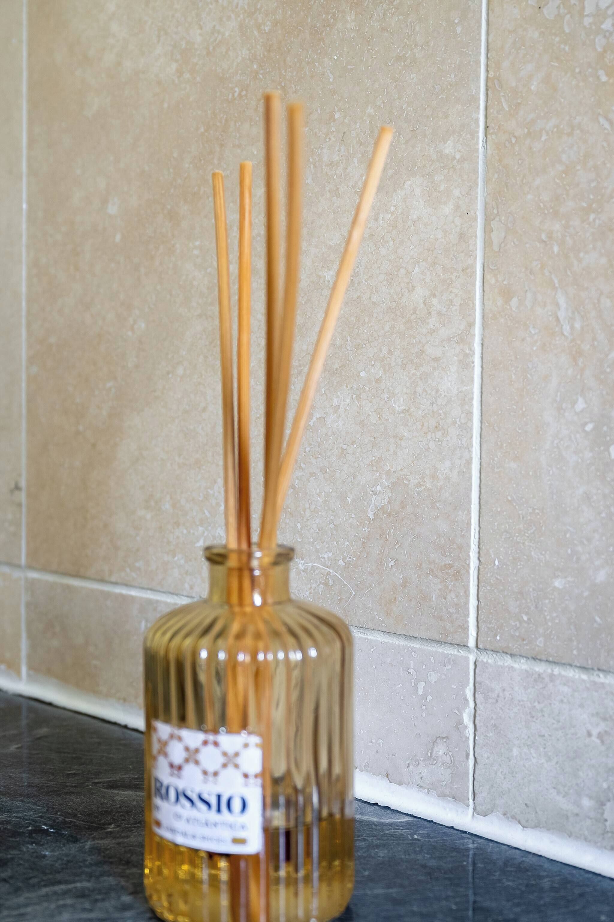 A bottle of Rossio cologne with reed sticks on a kitchen counter.