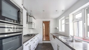 A modern kitchen with stainless steel appliances, white cabinetry, and a view to the adjacent room. - Elegant 3BR Victorian Retreat, Free Parking (Kingston Upon Thames)