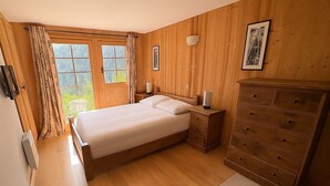 Ein Schlafzimmer mit Holzwänden, einem Bett, Nachttischen, einer Kommode und einem Fenster mit Vorhängen.